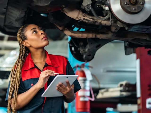 Female mechanic working under car with tablet